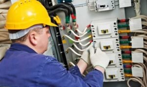 Electrician in hard hat working on electrical panel with wiring and circuit breakers, showcasing professional electrical services for residential and commercial needs.