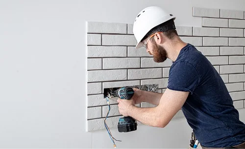 Electrician wearing a hard hat using a power drill to install electrical wiring in a residential setting, highlighting expertise in electrical services.
