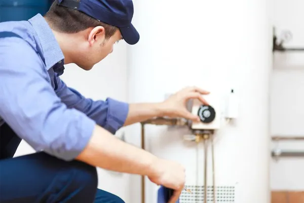 a plumber in a blue shirt kneeling, servicing a water heater unit, emphasizing plumbing repairs and installations in Miami Dade